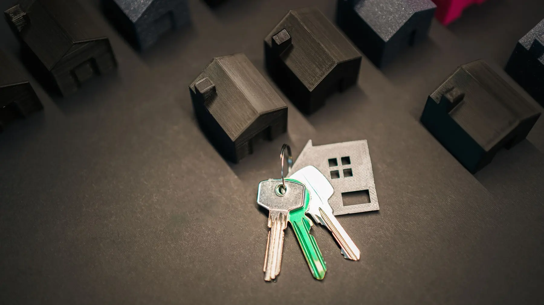 Small model houses and a set of keys on a dark table