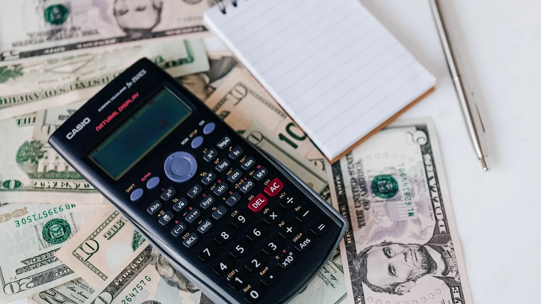 A calculator, a notepad and a pen on a white desk